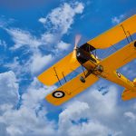 Yellow Tiger Moth aircraft flying in the sky, part of the Saskatchewan Aviation Museum collection